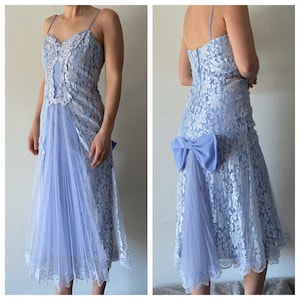 Puede incluir: Un vestido de encaje azul claro con una superposición de encaje blanco y un gran lazo azul en la espalda. El vestido tiene una falda de tul y un corpiño ajustado.