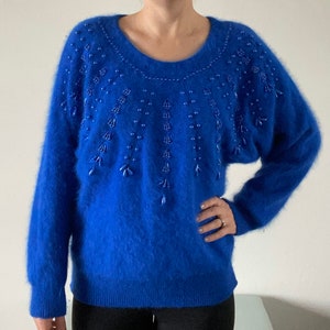 Può includere: Un maglione di lana blu reale con un collo decorato con perline. Le perline sono disposte a cascata.