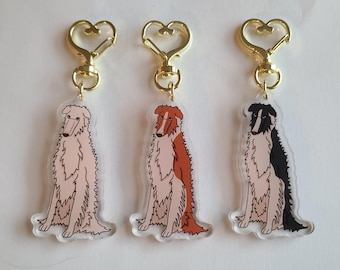 May include: Three dog-themed keychains with gold-colored heart-shaped clasps. Each keychain features a different color scheme: light pink, reddish-brown, and black and white. The dog illustrations are detailed and stylized.