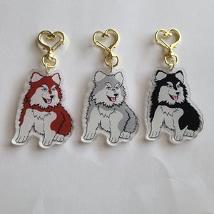 Pode incluir: Três chaveiros de acrílico com desenhos de cães husky de desenho animado em vermelho, cinza e preto. Cada chaveiro tem um fecho dourado em forma de coração. Os cães estão sentados com a língua de fora e têm marcas brancas.