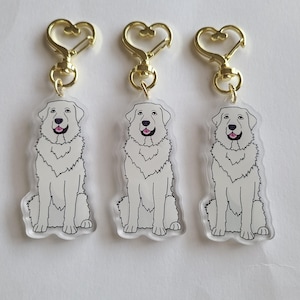 Puede incluir: Tres llaveros de acrílico transparente con un perro blanco sentado con un contorno negro. Cada llavero tiene un cierre dorado en forma de corazón. El perro tiene una lengua rosa y un cuello esponjoso. Los llaveros están sobre un fondo blanco.