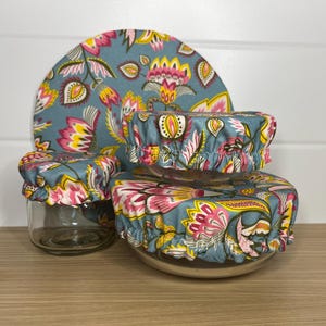May include: A collection of reusable bowl covers and a plate, displaying a teal floral design with pink, yellow, and white details. The covers are elasticated to fit various bowl sizes, and the plate is round. The set is designed for food storage.