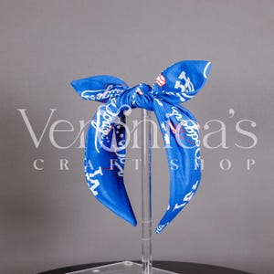 May include: Blue headband with a white baseball-themed print. The headband is tied in a knot at the top and has the text "Dodgers" on it.