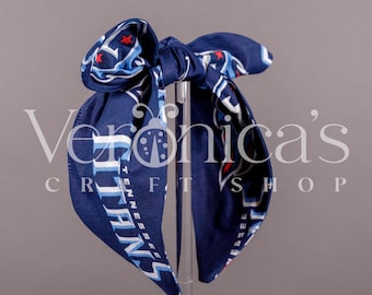 May include: A blue headband with a white and blue Tennessee Titans logo. The headband is tied in a bow at the top.