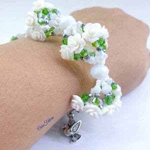 Puede incluir: Pulsera de cuentas blancas con cuentas verdes y plateadas, con detalles de flores blancas y un dije de paloma plateada.