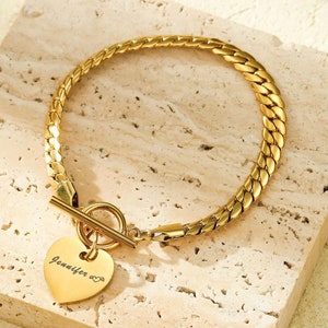 May include: Gold chain bracelet with a heart-shaped charm engraved with the name "Jennifer" and a small infinity symbol.