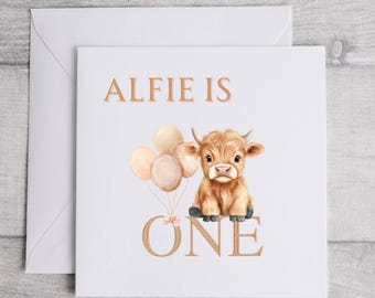 May include: Square white greeting card with the text "ALFIE IS ONE". The card features a watercolor illustration of a Highland cow holding balloons. The balloons are in shades of beige and peach.