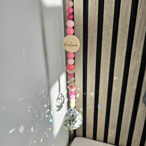 Könnte beinhalten: Rosa-weißer Perlen-Sonnenfänger mit einem Kristallprisma und einer Holzperle mit der Aufschrift "Paulina".