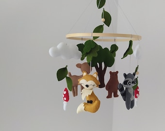 May include: A wooden baby mobile with felt woodland animals, including a fox, deer, bear, and raccoon. The mobile also features felt clouds and leaves.