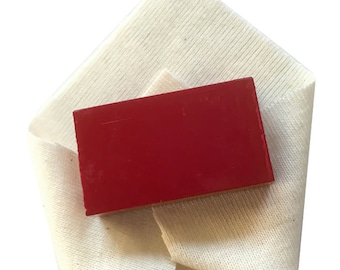 May include: A red rectangular block of wax on a white fabric background.
