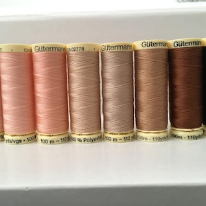 May include: Eight spools of Gütermann thread in a range of colours from pale pink to dark brown. Each spool is labelled with the brand name and thread type, with a capacity of 100 metres or 110 yards.