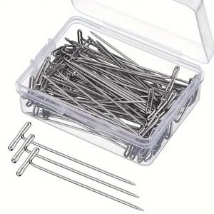 May include: A clear plastic box filled with silver T-pins. The box is open and there are a few T-pins outside of the box.