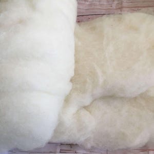 May include: Close-up of white fluffy wadding material, suitable for stuffing pillows, crafts, or other projects. The wadding is soft and cloud-like, with a slightly off-white hue. The texture appears dense and uniform, suitable for various applications.