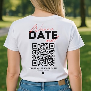 Op de afbeelding: Wit T-shirt met de tekst "Wanna DATE me?" in zwart en rood, een QR-code en de zin "TRUST ME, IT'S WORTH IT!". Het T-shirt is gemaakt van een zacht materiaal en is geschikt voor vrijetijdskleding.