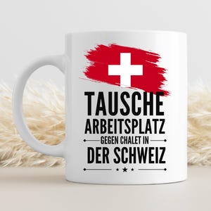May include: White ceramic mug with a Swiss flag design. The mug features a red brushstroke with a white cross and the German text "TAUSCHE ARBEITSPLATZ GEGEN CHALET IN DER SCHWEIZ."