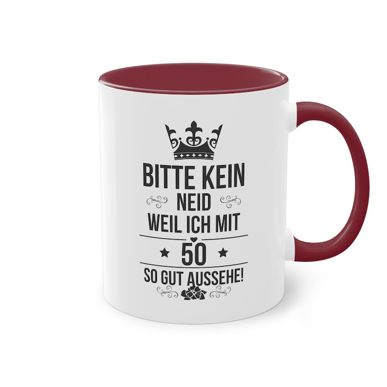 Pode incluir: Caneca de cer&acirc;mica branca com interior e al&ccedil;a bord&ocirc;. A caneca apresenta um texto preto que diz "BITTE KEIN NEID WEIL ICH MIT 50 SO GUT AUSSEHE!" com um design de coroa e estrela. Um elemento floral decorativo tamb&eacute;m est&aacute; presente.