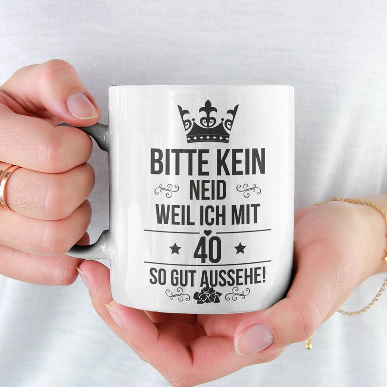 May include: White ceramic mug with a black crown, text that reads "Bitte kein Neid weil ich mit 40 so gut aussehe!" and a small heart.