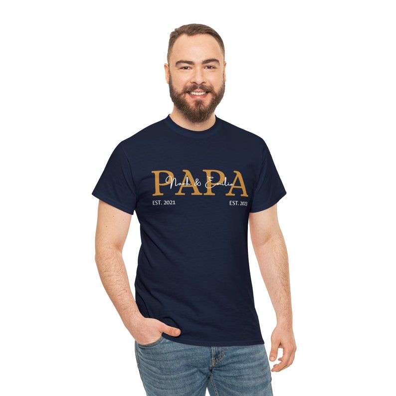 Puede incluir: Una camiseta azul marino con la palabra "PAPA" en letras doradas. El texto "Noah & Edie" est&aacute; escrito en blanco en cursiva debajo de la palabra "PAPA". El texto "EST. 2021" est&aacute; escrito en blanco debajo del lado izquierdo de la palabra "PAPA" y el texto "EST. 2023" est&aacute; escrito en blanco debajo del lado derecho de la palabra "PAPA".