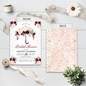 May include: A white bridal shower invitation with a gold and white polka dot background. A gold umbrella with burgundy and white flowers is at the top of the invitation. The text "Bridal Shower" is in burgundy and the text "Kristen Chambers" is in black. The date and time of the shower are listed below. The back of the invitation has a pink and gold floral pattern.