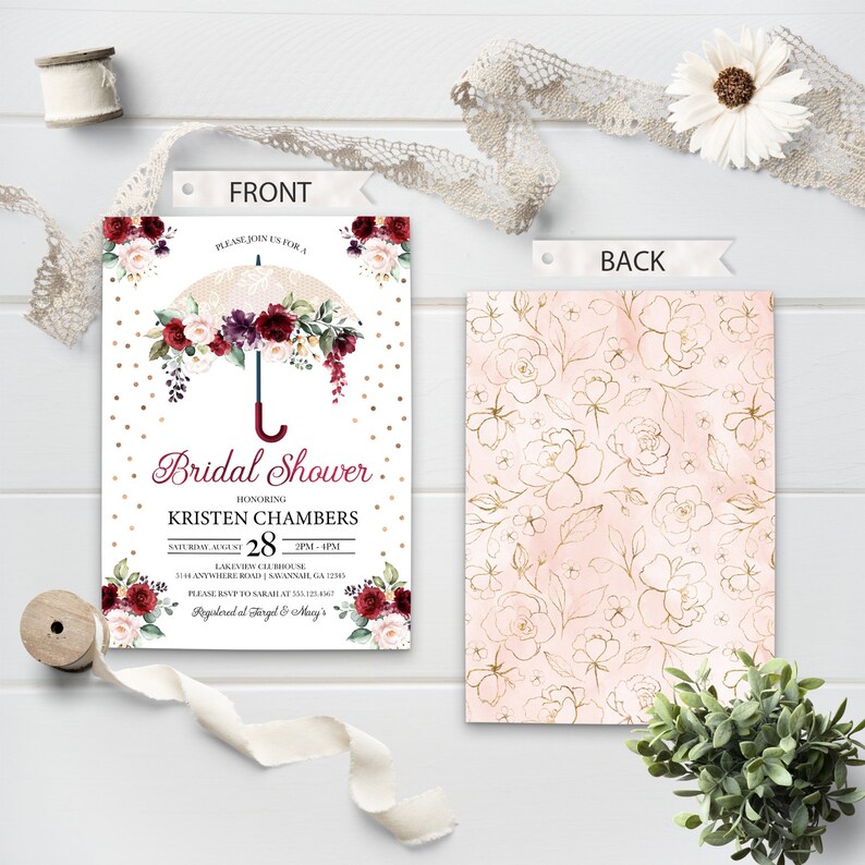 May include: A white bridal shower invitation with a gold and white polka dot background. A gold umbrella with burgundy and white flowers is at the top of the invitation. The text "Bridal Shower" is in burgundy and the text "Kristen Chambers" is in black. The date and time of the shower are listed below. The back of the invitation has a pink and gold floral pattern.