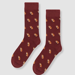 May include: A pair of burgundy socks featuring a repeating pattern of orange and white foxes. The socks have a ribbed cuff and a solid burgundy colour on the cuff and toe.
