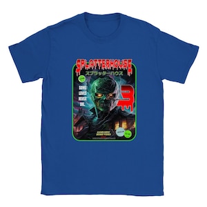 Può includere: Una t-shirt blu con una grafica di una scatola VHS per il film horror "Splatterhouse 3". La scatola presenta un mostro verde con occhi rossi luminosi e il testo "Splatterhouse" e "スプラッターハウス" in rosso. Il testo "Some Loves Never Die." è in verde.