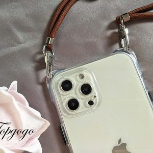 May include: A clear phone case with a brown strap attached. The case has a white phone inside with a camera lens and an Apple logo.