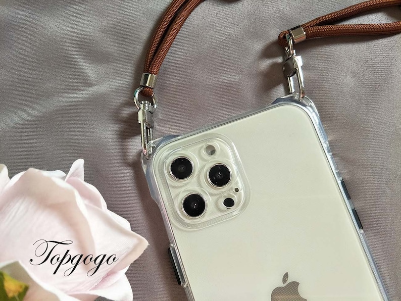May include: A clear phone case with a brown strap attached. The case has a white phone inside with a camera lens and an Apple logo.