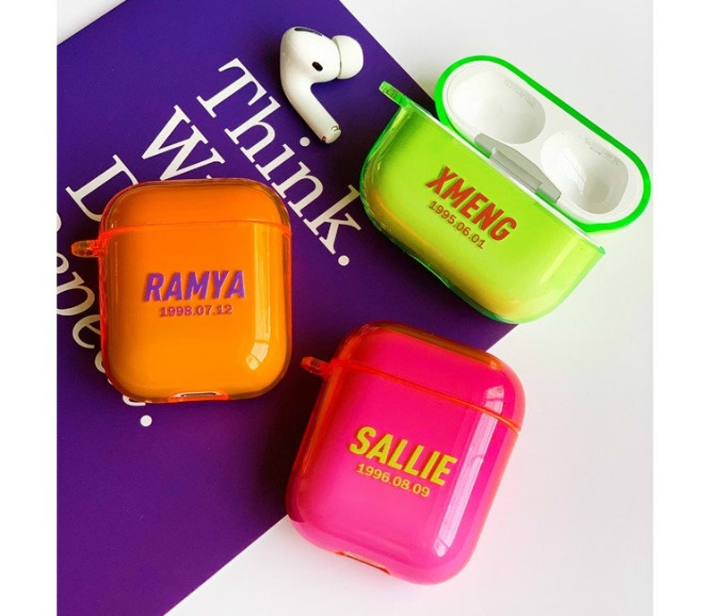K&ouml;nnte beinhalten: Drei transparente AirPod-H&uuml;llen aus Kunststoff mit verschiedenen durchscheinenden Hintergr&uuml;nden. Die H&uuml;llen tragen Namen und Daten, die darauf gedruckt sind: "RAMYA 1998.07.12" in Lila auf einer orangenen H&uuml;lle, "XMENG 1995.06.01" in Rot auf einer gelben H&uuml;lle und "SALLIE 1996.08.09" in Gelb auf einer rosa H&uuml;lle.