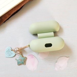 May include: A light green silicone case for wireless earbuds with a gold chain and charm attached. The charm is a blue starfish with a heart-shaped tag that says "Alice & Luna".