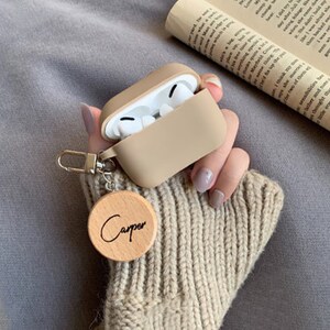 May include: A beige silicone case for wireless earbuds with a wooden keychain that says "Carper".