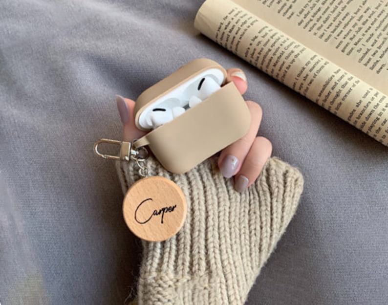 May include: A beige silicone case for wireless earbuds with a wooden keychain that says "Carper".
