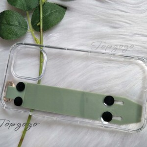 May include: Clear phone case with a sage green strap and black circular accents. The case has a gold-colored metal loop and the text "Topgogo" is visible. The case is designed to protect a phone.