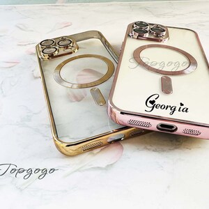Puede incluir: Dos fundas transparentes para tel&eacute;fono con detalles dorados. La funda de la izquierda tiene un anillo dorado alrededor del objetivo de la c&aacute;mara. La funda de la derecha tiene un anillo dorado alrededor del objetivo de la c&aacute;mara y un fondo blanco con el texto "Topgogo" y "Georgia" en negro.