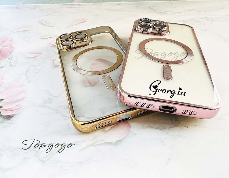 Puede incluir: Dos fundas transparentes para tel&eacute;fono con detalles dorados. La funda de la izquierda tiene un anillo dorado alrededor del objetivo de la c&aacute;mara. La funda de la derecha tiene un anillo dorado alrededor del objetivo de la c&aacute;mara y un fondo blanco con el texto "Topgogo" y "Georgia" en negro.
