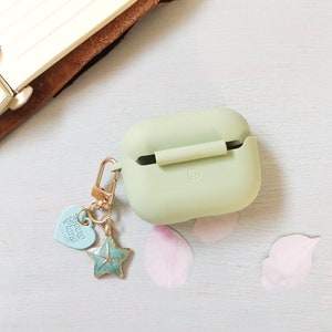 May include: A light green silicone case for wireless earbuds with a gold chain and charm. The charm is a blue starfish with a heart-shaped charm that says "Good Vibes".