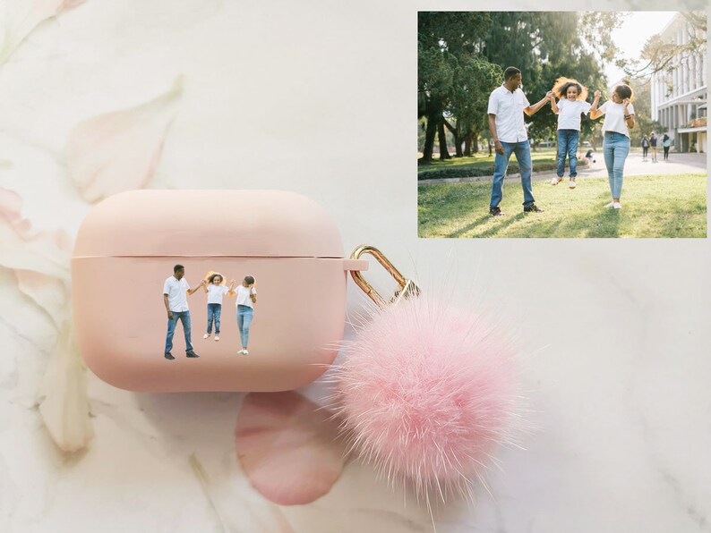 May include: A pink Airpods case with a fuzzy pink pom-pom keychain. The case has a photo of a family of three, a man and two girls, holding hands and smiling.