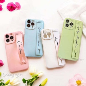 May include: Four phone cases with a built-in phone grip. The cases are in pink, blue, white, and green. The phone grip has a customizable text option. The text on the cases reads "Custom", "Love: Jennifer", "Love:", and "Lucky Angelina".