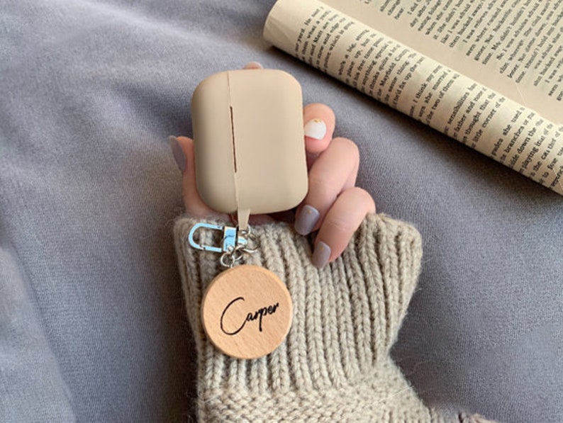 May include: A beige silicone case for wireless earbuds with a wooden keychain that says "Carper".