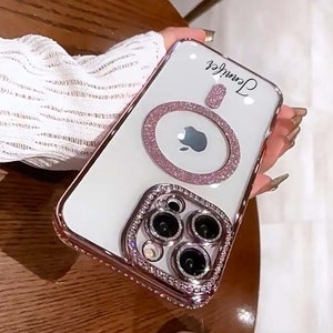 Op de afbeelding: Witte iPhone-hoes met een roze, glinsterende ringhouder en een met diamanten bezette camera-lensafdekking. Op de achterkant van de hoes staat de naam "Jennifer".
