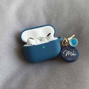 May include: A blue silicone case for wireless earbuds with a gold chain and a blue charm with the name "Mikeo" written on it.