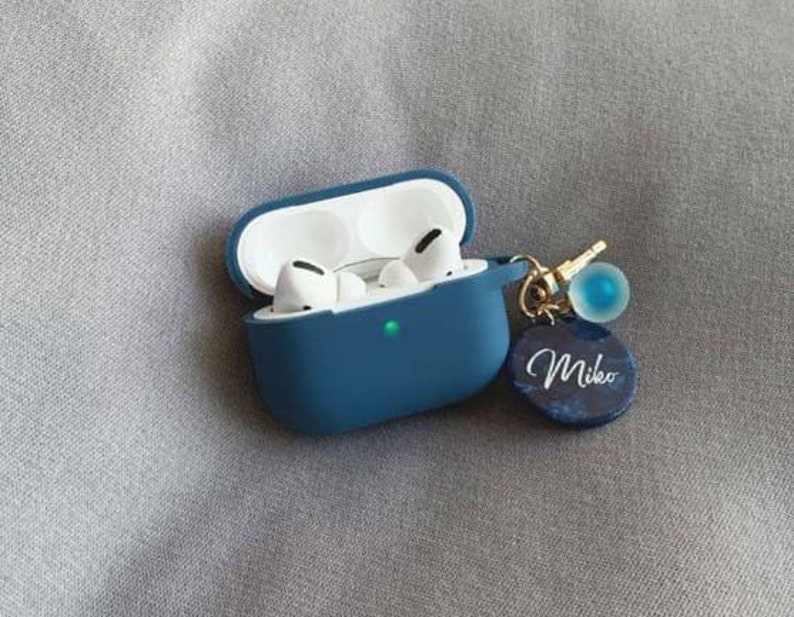 May include: A blue silicone case for wireless earbuds with a gold chain and a blue charm with the name "Mikeo" written on it.