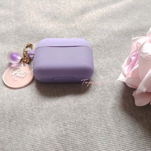 May include: A lavender silicone case for wireless earbuds with a gold chain and a pink charm with the word "Kelli" engraved on it.
