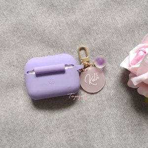 May include: A purple silicone case for wireless earbuds with a gold chain and a pink personalized charm that says "Kolbi".