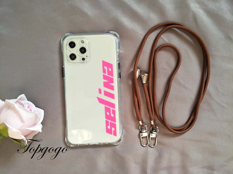 May include: A clear phone case with a pink "99J" logo and a brown phone strap with gold clasps.