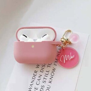 May include: Pink Airpods case with a gold keychain featuring a pink charm and a pink circle with the name "Mike" written in white.
