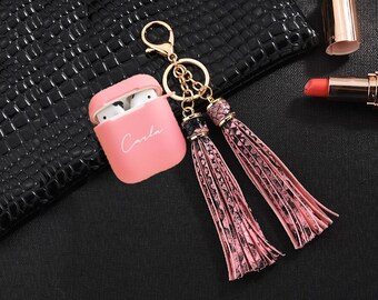 May include: Pink Airpods case with the name "Carla" written on it, attached to a gold keychain with two pink tassel charms.