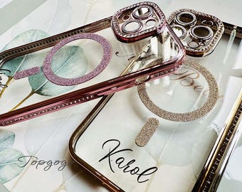 May include: Two clear phone cases with rose gold trim and rhinestones. The cases have glitter accents and the names "Linda" and "Karol" written on them.