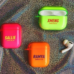 K&ouml;nnte beinhalten: Drei farbige Airpod-H&uuml;llen mit personalisierten Namen und Geburtsdaten. Die H&uuml;llen sind gr&uuml;n, pink und orange. Die Namen sind "Xmeng 1995.06.01", "Sallie 1996.08.09" und "Ramya 1998.07.12".
