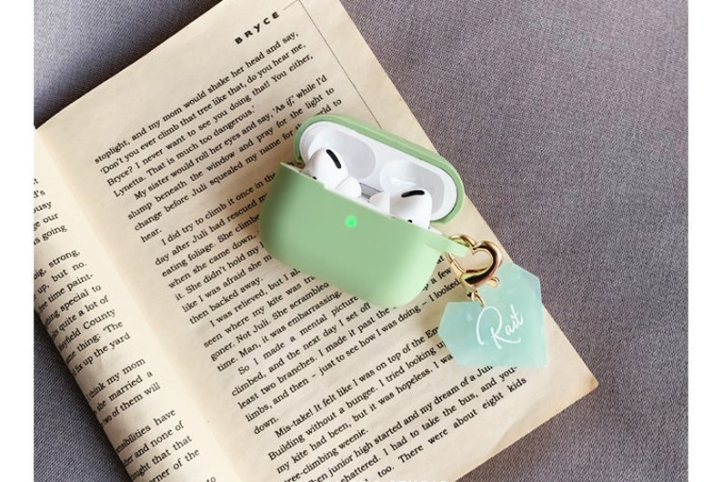 May include: A light green protective case for wireless earbuds with a gold keychain attached. The keychain has a light green tag with the word "Rait" written in cursive.
